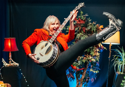 Eliza Mary Doyle wearing a red jacket and black cowboy boots, and holding her banjo.